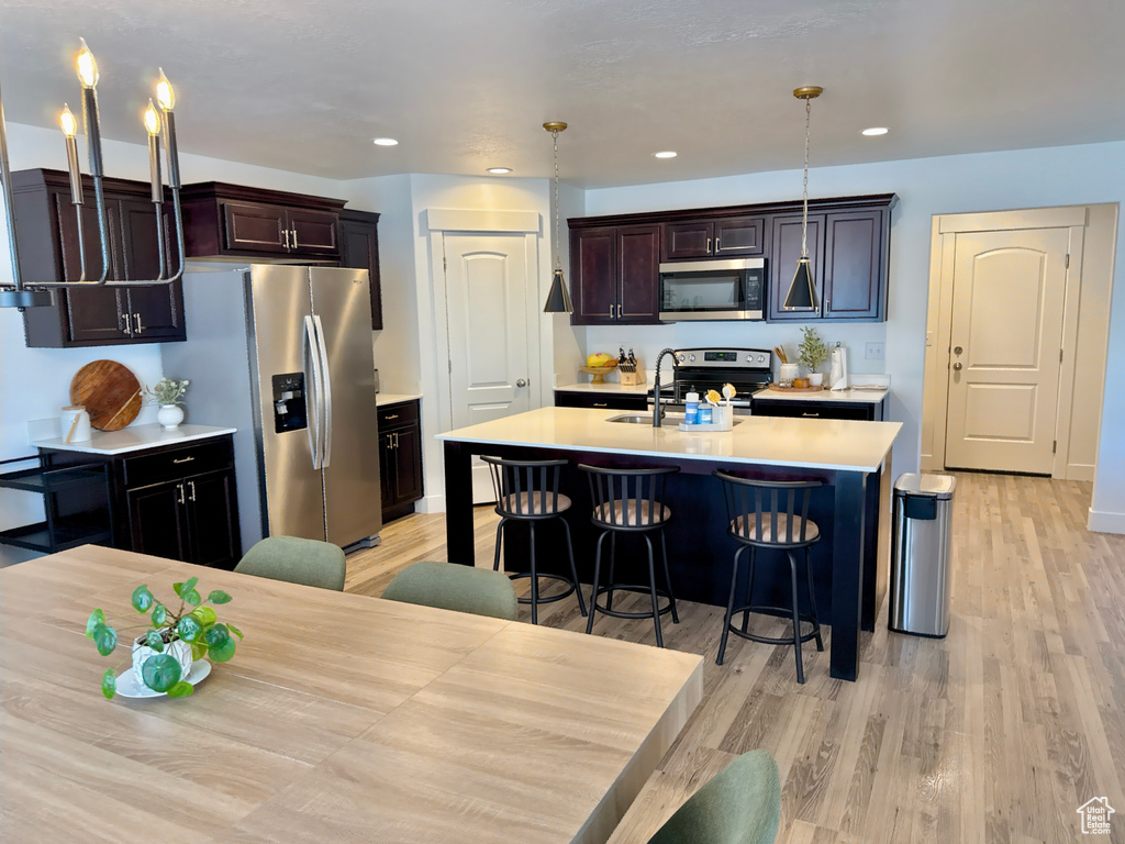 Kitchen featuring stainless steel appliances, a sink, light countertops, light wood-type flooring, and a kitchen breakfast bar