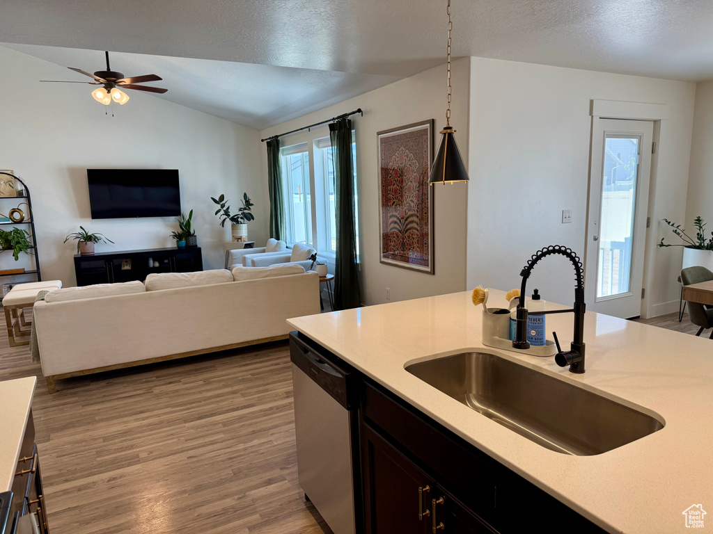 Kitchen featuring dishwasher, a sink, light countertops, light wood-style flooring, and vaulted ceiling
