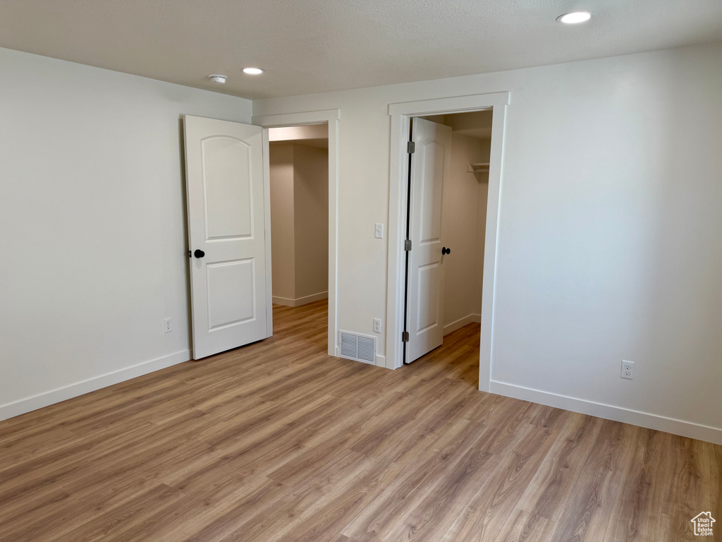 Unfurnished bedroom with recessed lighting, light wood-type flooring, baseboards, and a walk in closet