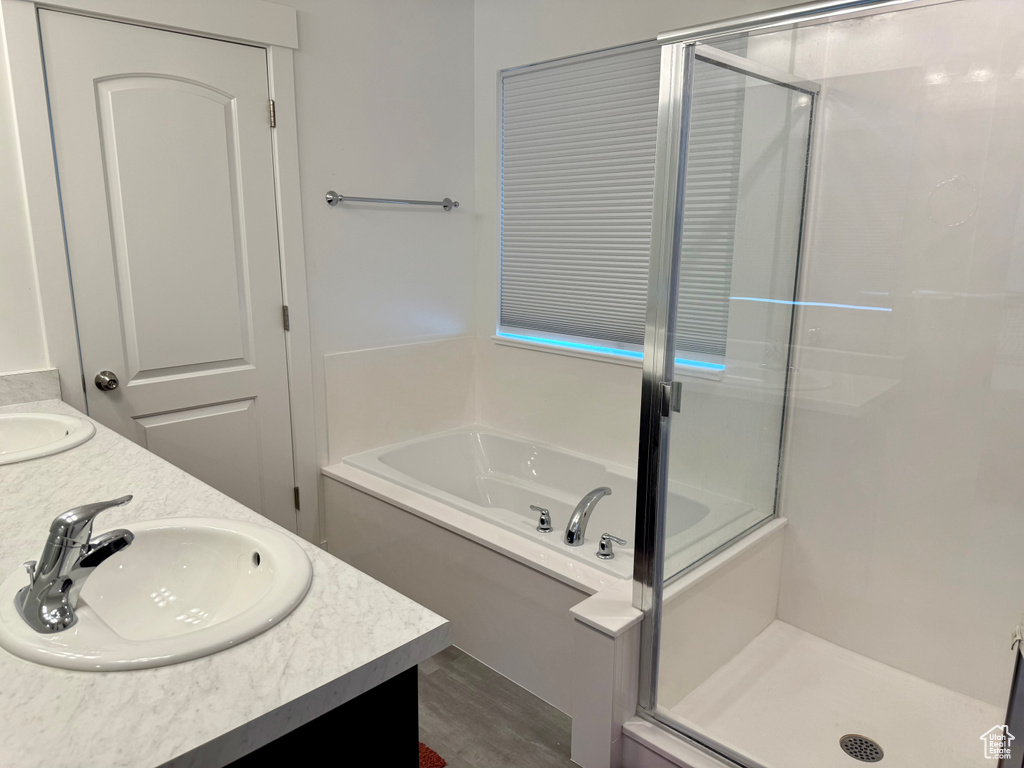 Bathroom with a stall shower, a garden tub, double vanity, and wood finished floors