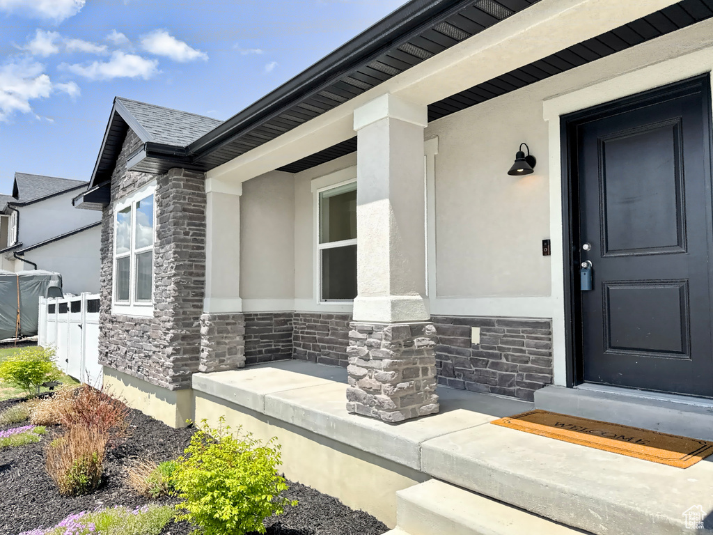 Entrance to property with stone siding, stucco siding, fence, and covered porch