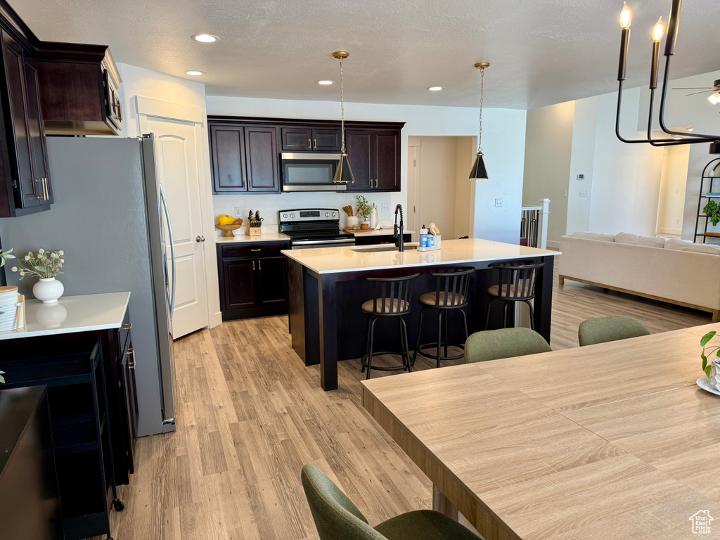 Kitchen with appliances with stainless steel finishes, light countertops, light wood-style floors, a kitchen bar, and a sink