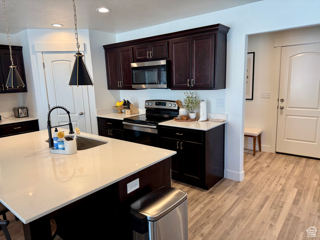 Kitchen with appliances with stainless steel finishes, a sink, recessed lighting, a breakfast bar area, and light wood-type flooring