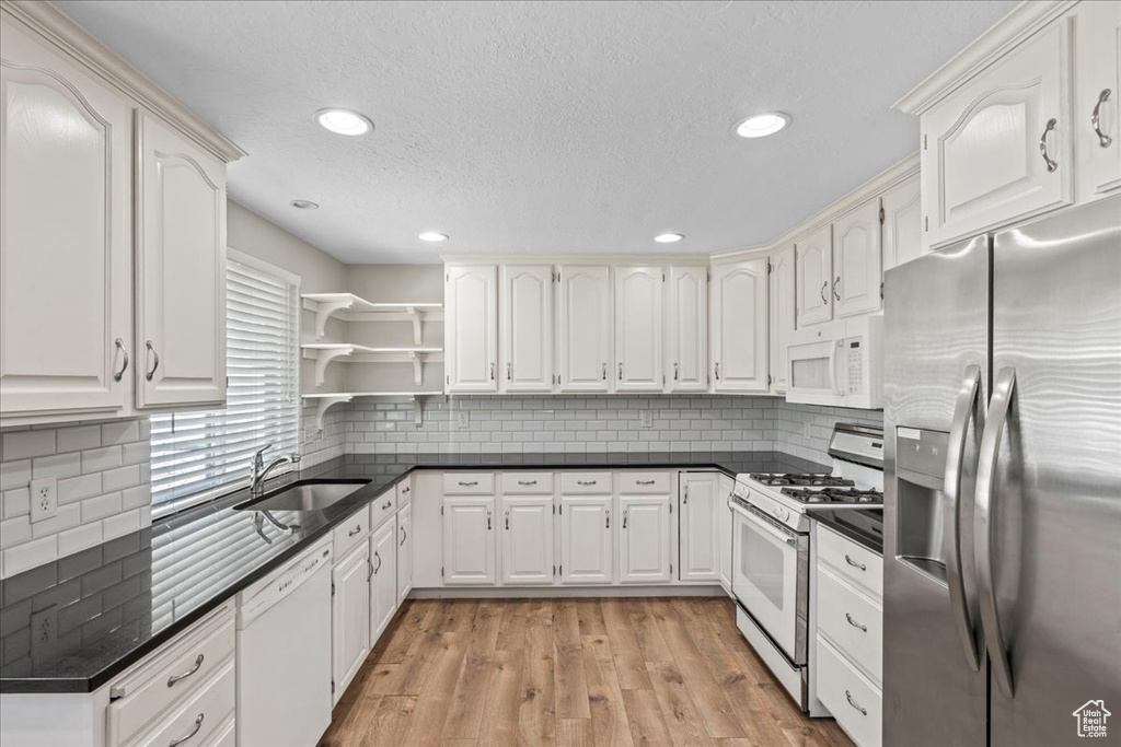 Kitchen with white appliances, dark countertops, a sink, open shelves, and recessed lighting