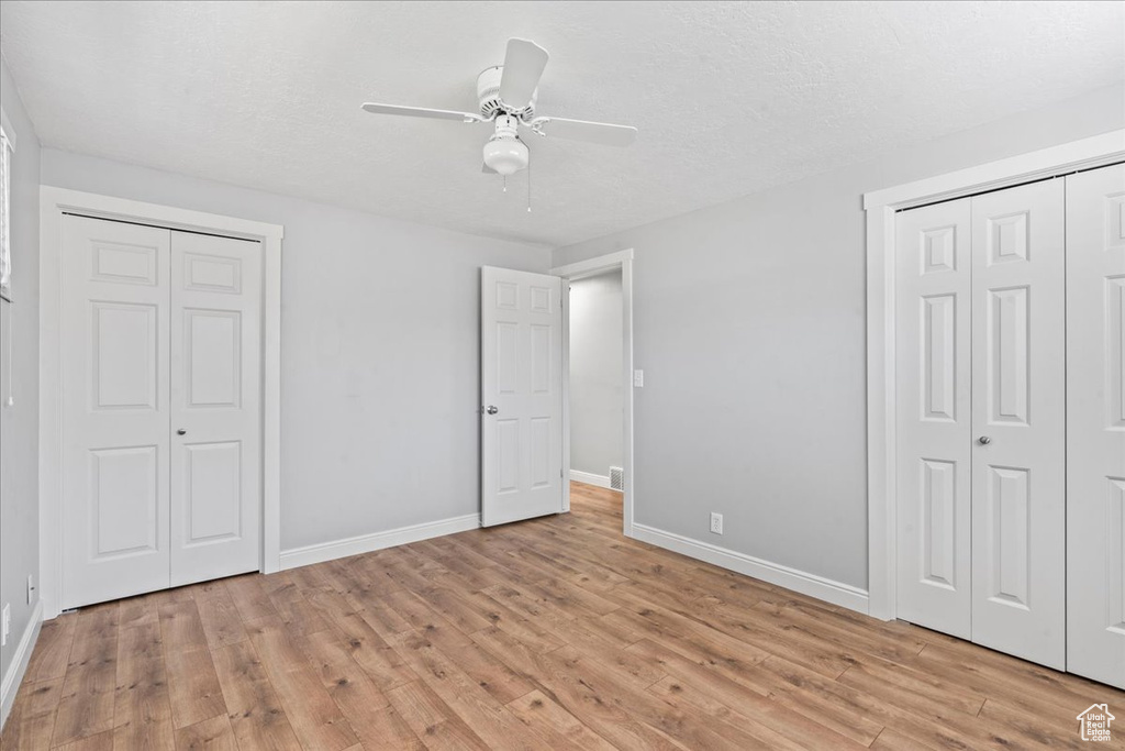 Unfurnished bedroom with light wood-type flooring, baseboards, two closets, a ceiling fan, and a textured ceiling