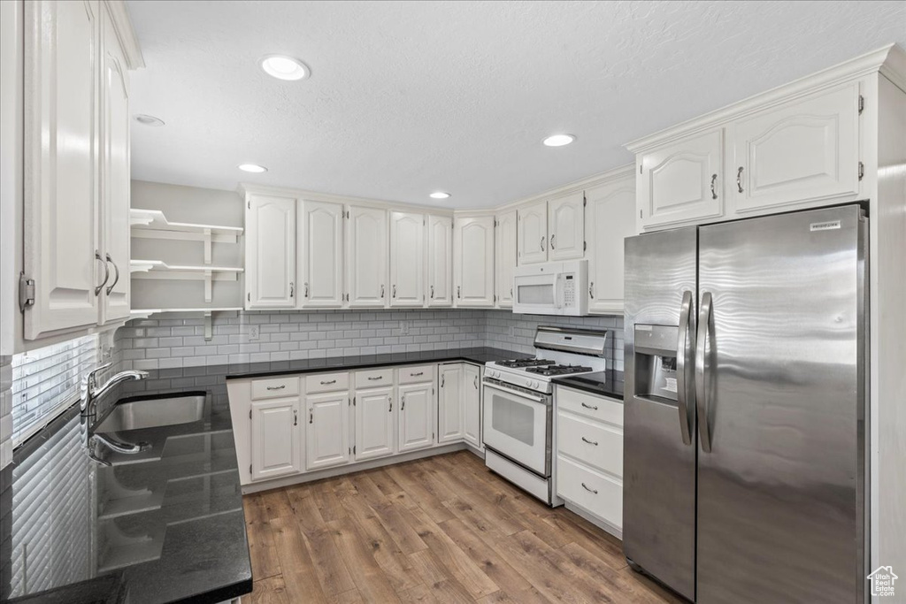 Kitchen with white appliances, dark countertops, open shelves, tasteful backsplash, and white cabinets