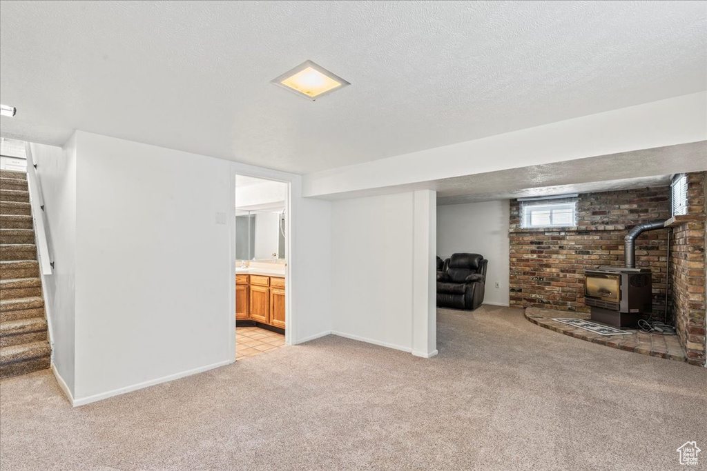 Basement featuring a wood stove, light carpet, stairs, baseboards, and a textured ceiling