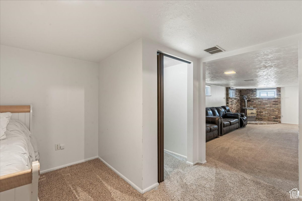 Bedroom with light carpet, a textured ceiling, baseboards, and a wood stove