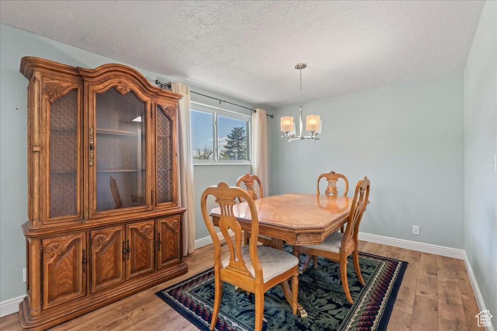 Dining space featuring a chandelier, light wood-style flooring, a textured ceiling, and baseboards