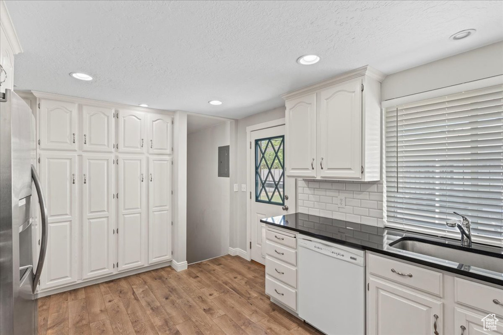 Kitchen featuring white dishwasher, a sink, dark countertops, baseboards, and white cabinetry