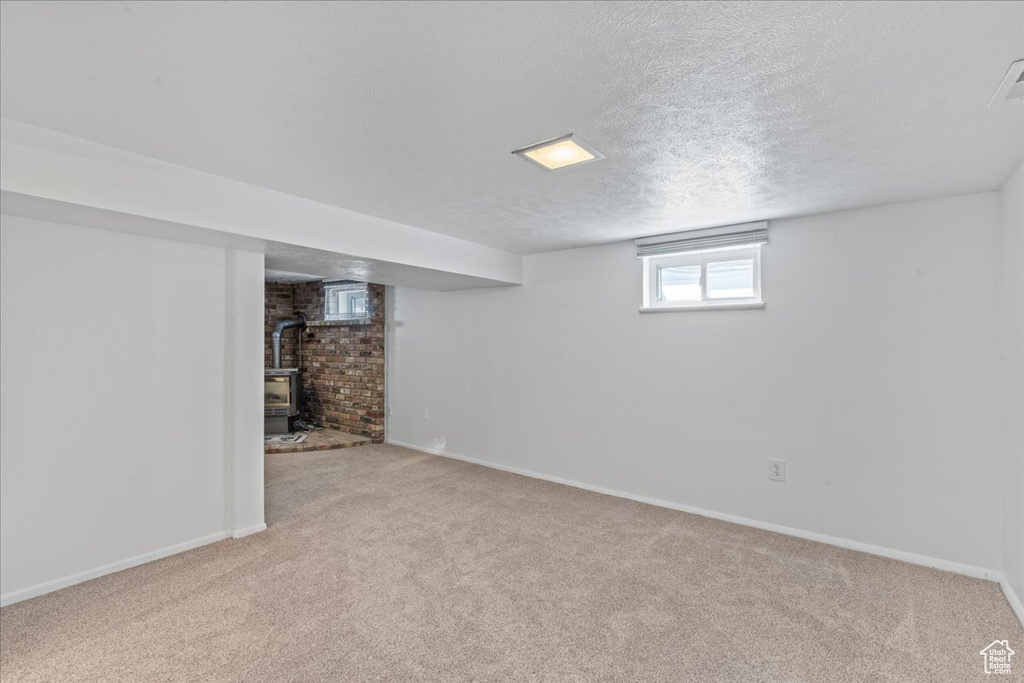 Below grade area featuring a wood stove, light carpet, a textured ceiling, and baseboards