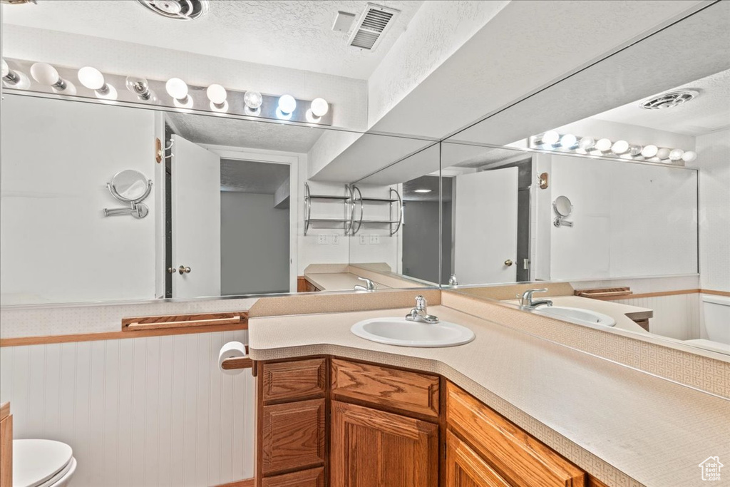 Bathroom with toilet, a textured ceiling, vanity, and wainscoting