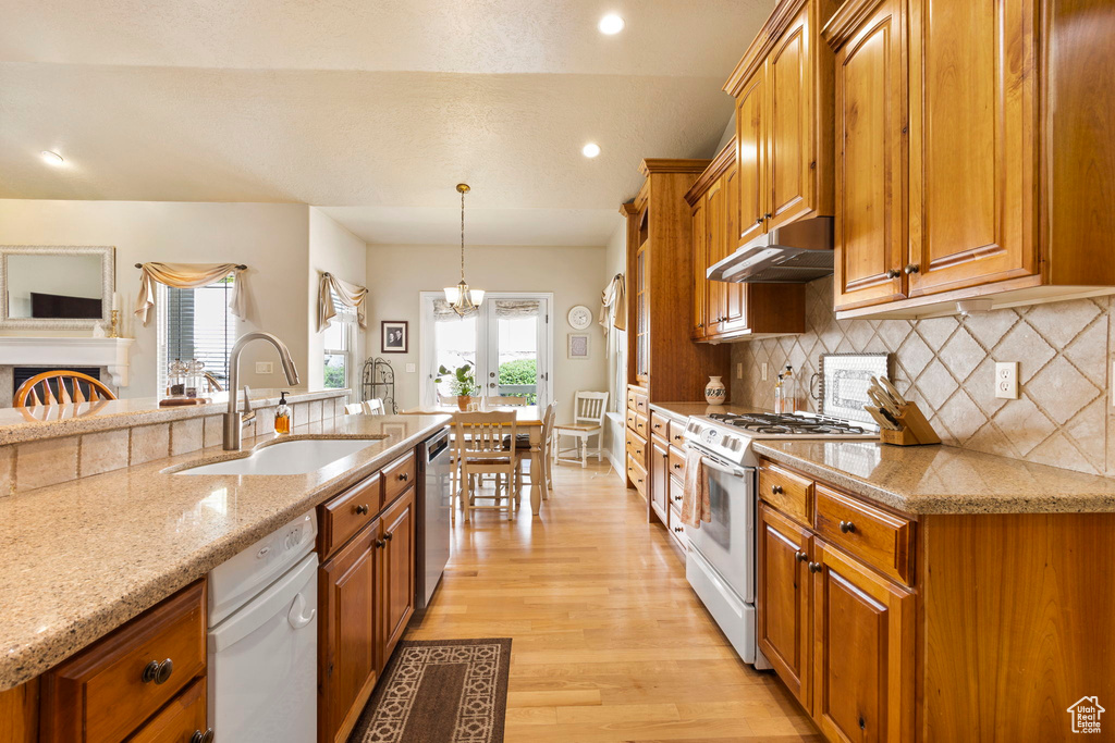 Kitchen featuring white gas range, brown cabinets, dishwasher, a sink, and under cabinet range hood