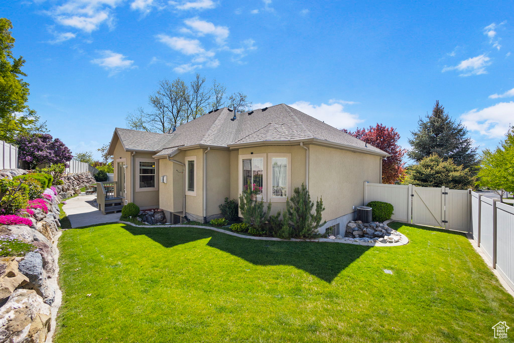 View of front of house with a front yard, cooling unit, a fenced backyard, stucco siding, and a gate
