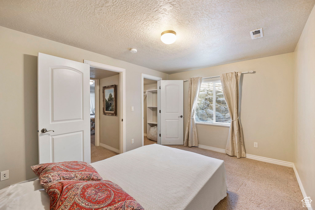 Bedroom with light carpet, a textured ceiling, baseboards, a spacious closet, and visible vents
