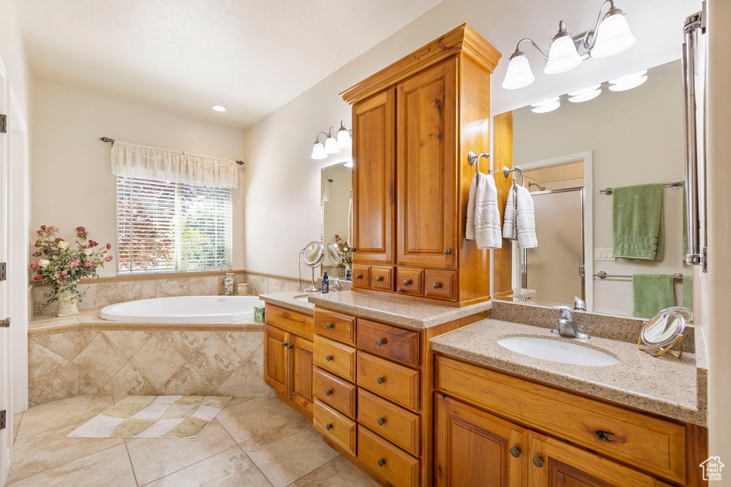 Bathroom featuring a garden tub, double vanity, tile patterned floors, a sink, and a stall shower