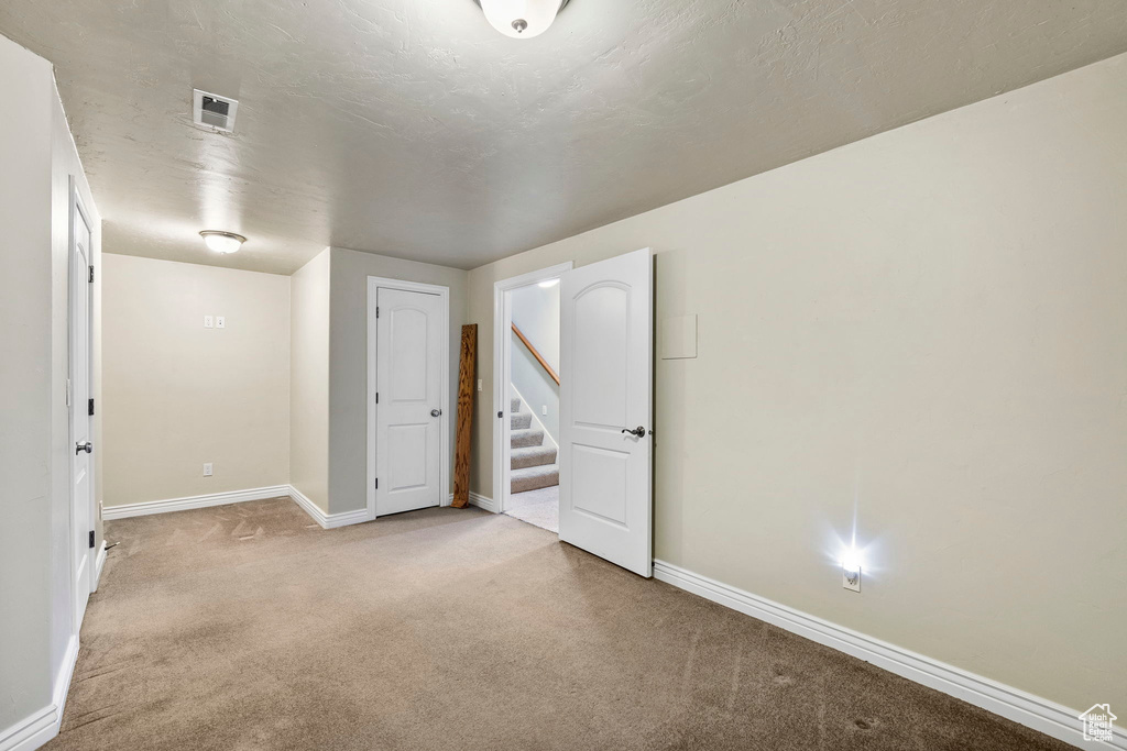 Empty room with stairs, baseboards, visible vents, and light carpet