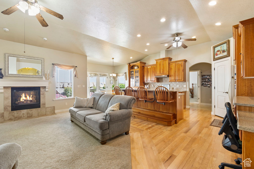 Living area with a fireplace, arched walkways, ceiling fan with notable chandelier, baseboards, and vaulted ceiling