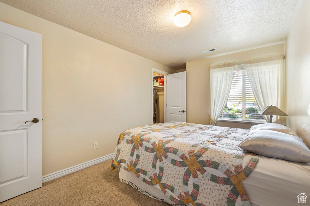 Bedroom with a textured ceiling, visible vents, baseboards, and carpet
