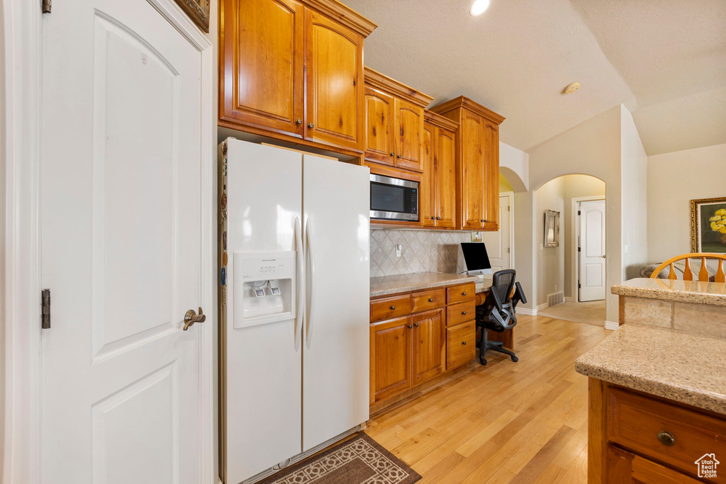 Kitchen featuring backsplash, arched walkways, built in desk, stainless steel microwave, and white fridge with ice dispenser