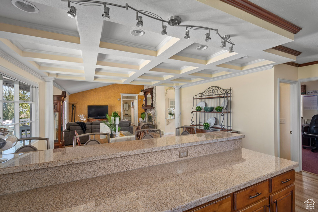 Kitchen with ornate columns, coffered ceiling, wood finished floors, brown cabinetry, and crown molding