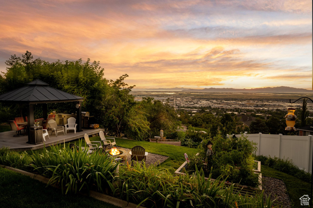 Yard at dusk featuring an outdoor fire pit, a gazebo, a deck with mountain view, and fence