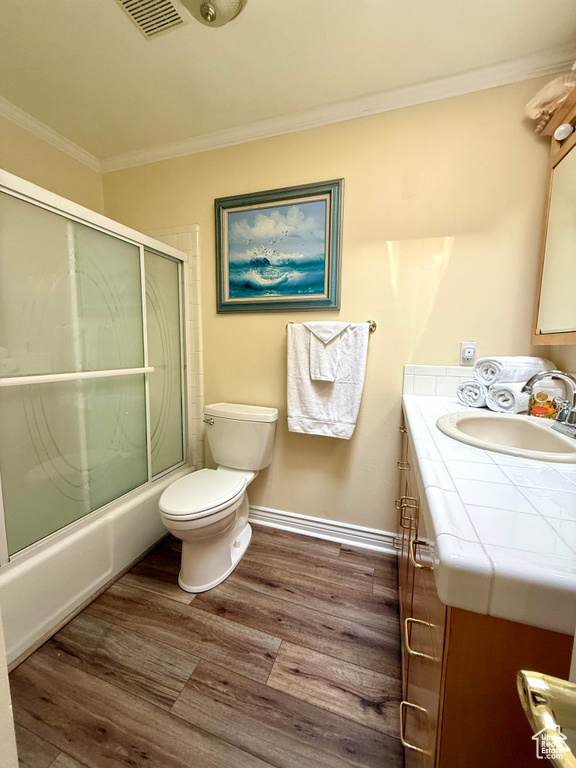 Full bathroom featuring ornamental molding, vanity, wood finished floors, toilet, and shower / bath combination with glass door
