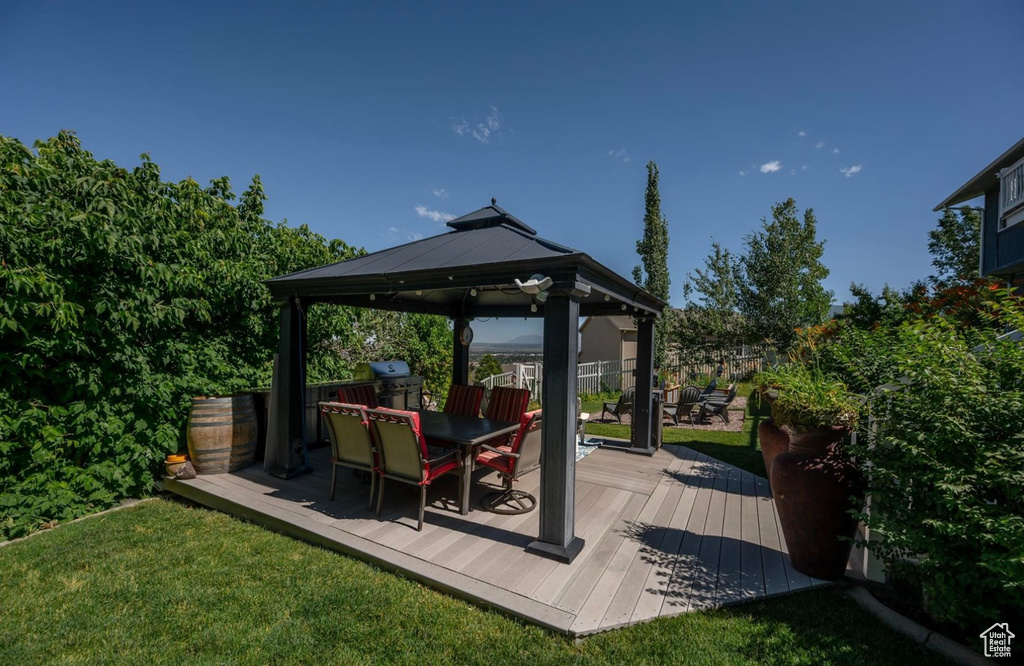 Wooden terrace featuring a gazebo, outdoor dining space, a lawn, and area for grilling