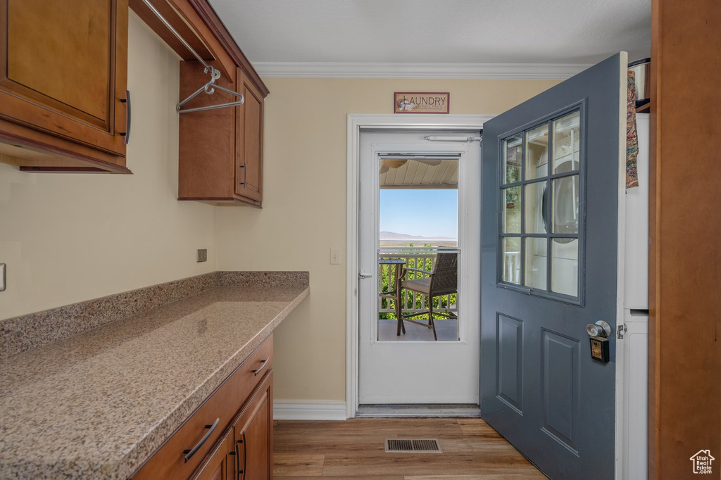 Laundry area with light wood-type flooring, baseboards, and ornamental molding