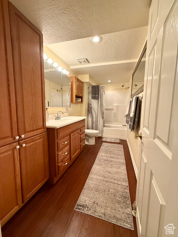 Full bath featuring a textured ceiling, wood finished floors, toilet, shower / bath combination with curtain, and vanity