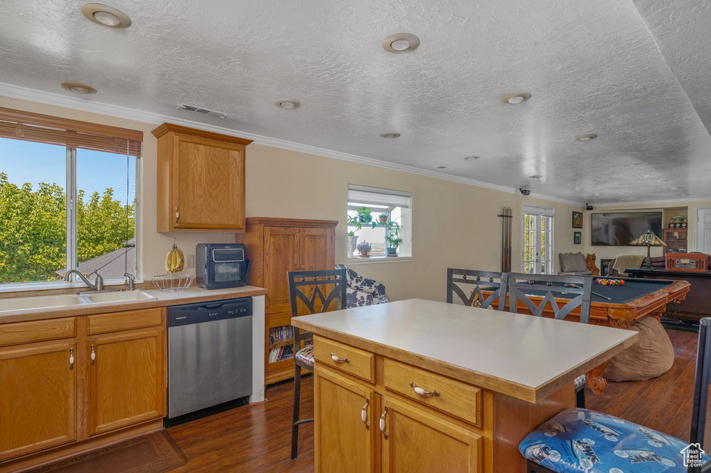 Kitchen featuring stainless steel dishwasher, a sink, a breakfast bar, dark wood-type flooring, and crown molding