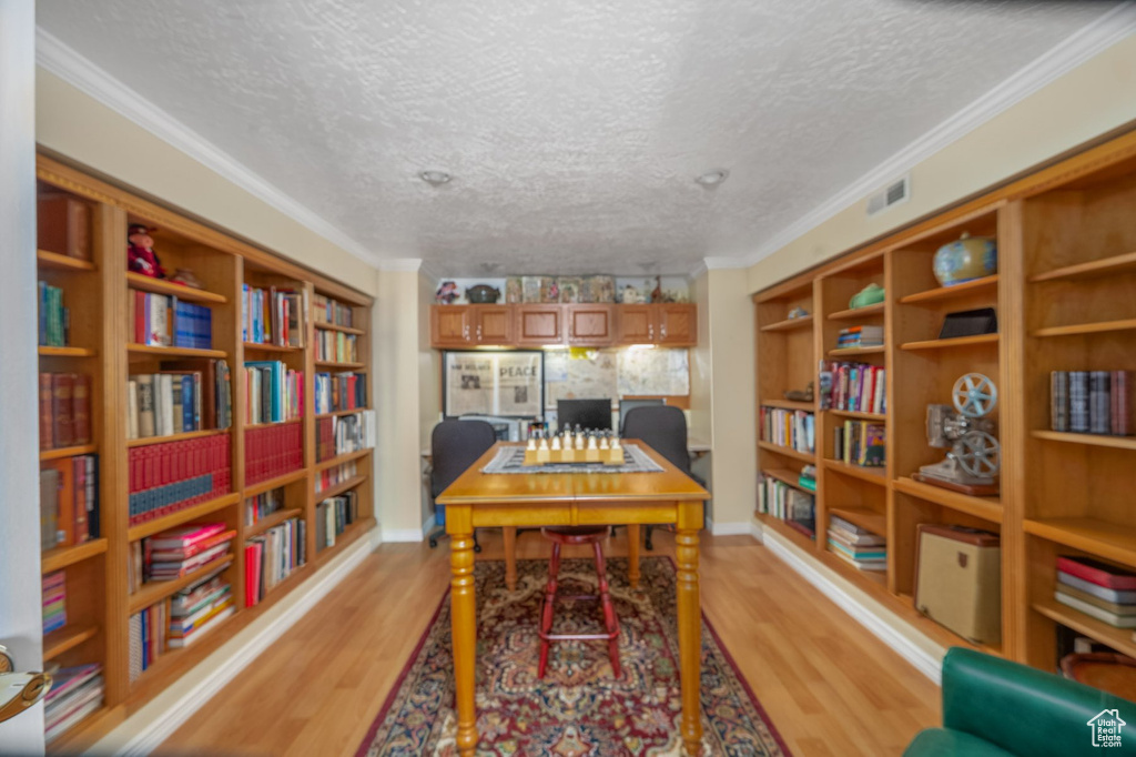 Office featuring light wood-type flooring, a textured ceiling, ornamental molding, and bookshelves