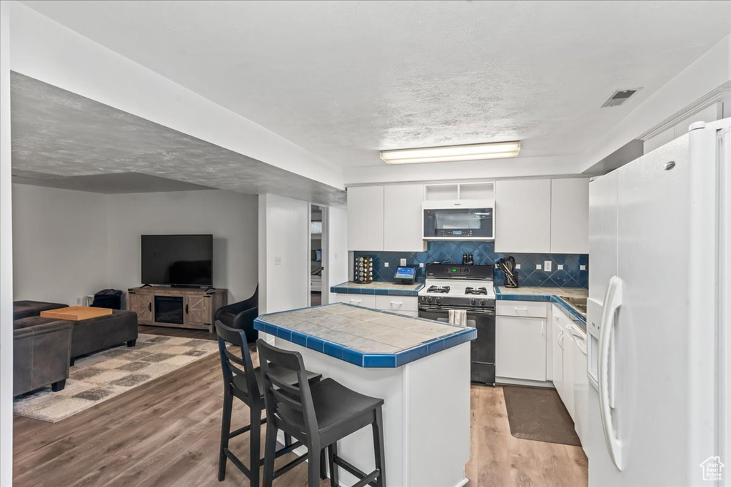 Kitchen featuring white fridge with ice dispenser, gas stove, tile counters, white cabinets, and light wood-type flooring
