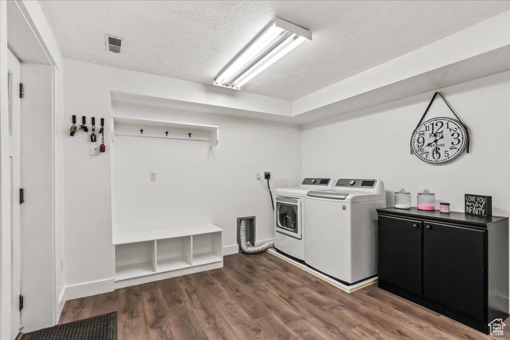 Washroom with washing machine and dryer, a textured ceiling, cabinet space, dark wood-style flooring, and baseboards