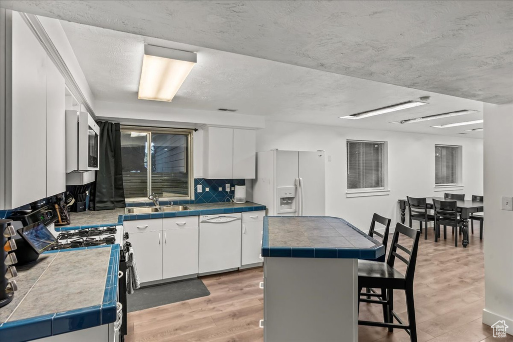 Kitchen featuring white appliances, a sink, white cabinets, light wood finished floors, and a textured ceiling
