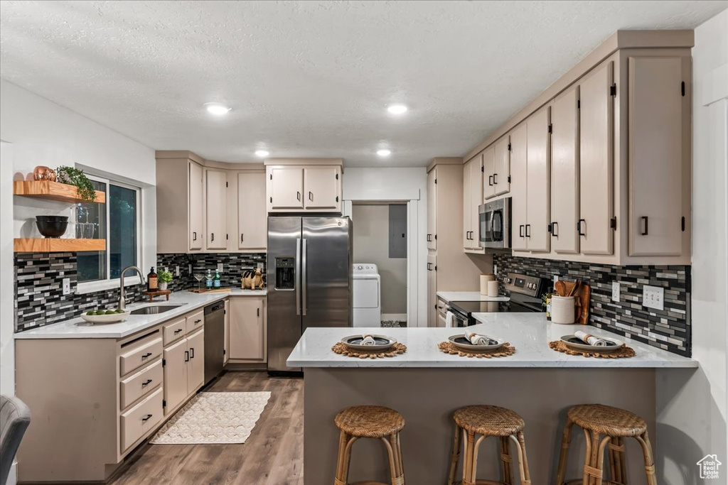 Kitchen with stainless steel appliances, a sink, a peninsula, dark wood finished floors, and washer / dryer