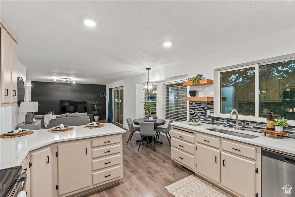 Kitchen with stainless steel dishwasher, a sink, light countertops, stove, and hanging light fixtures
