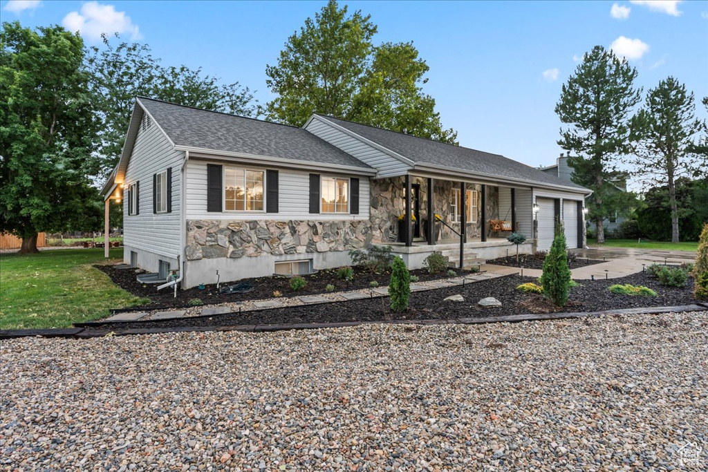 Ranch-style home with covered porch, a garage, driveway, a chimney, and stone siding