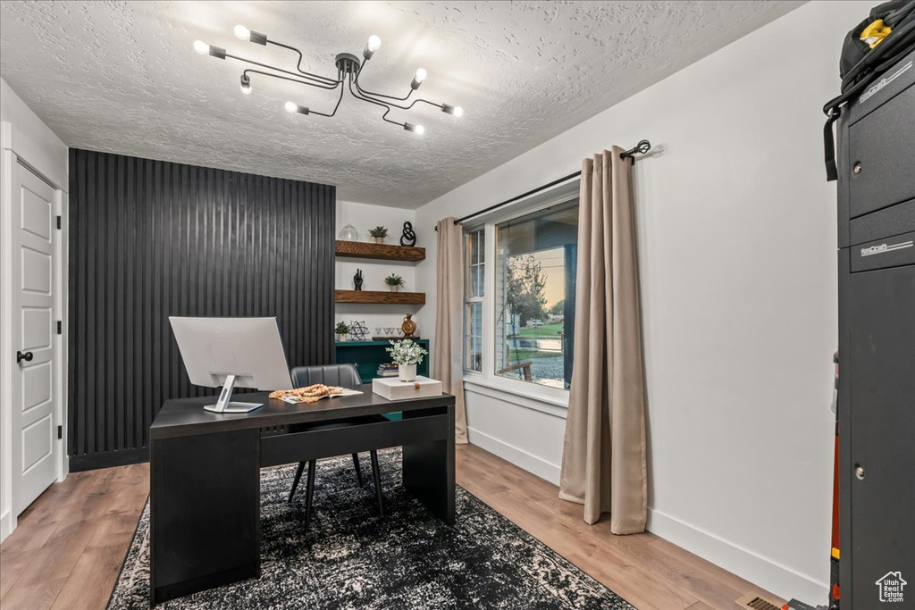 Office space featuring a chandelier, light wood finished floors, baseboards, and a textured ceiling