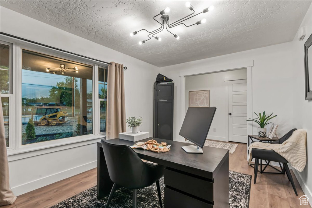 Office space featuring a chandelier, a textured ceiling, light wood-style flooring, and baseboards