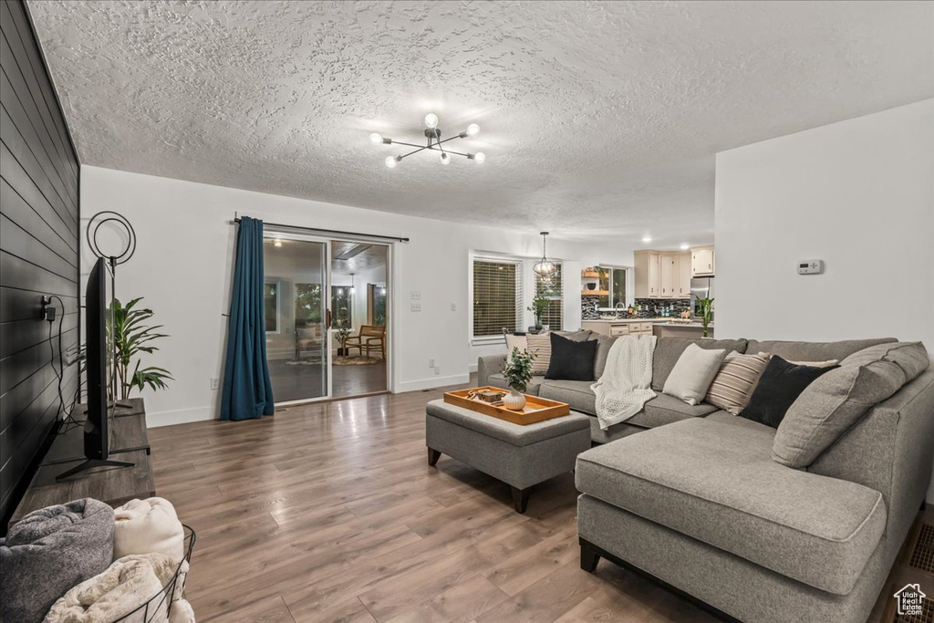 Living area featuring a chandelier, wood finished floors, baseboards, and a textured ceiling