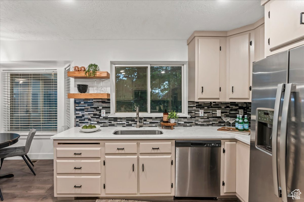 Kitchen with stainless steel appliances, a sink, light countertops, tasteful backsplash, and dark wood-style floors