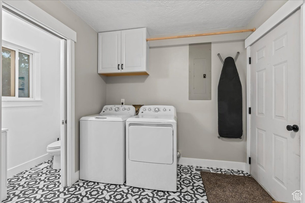 Washroom with electric panel, cabinet space, baseboards, washer and dryer, and a textured ceiling