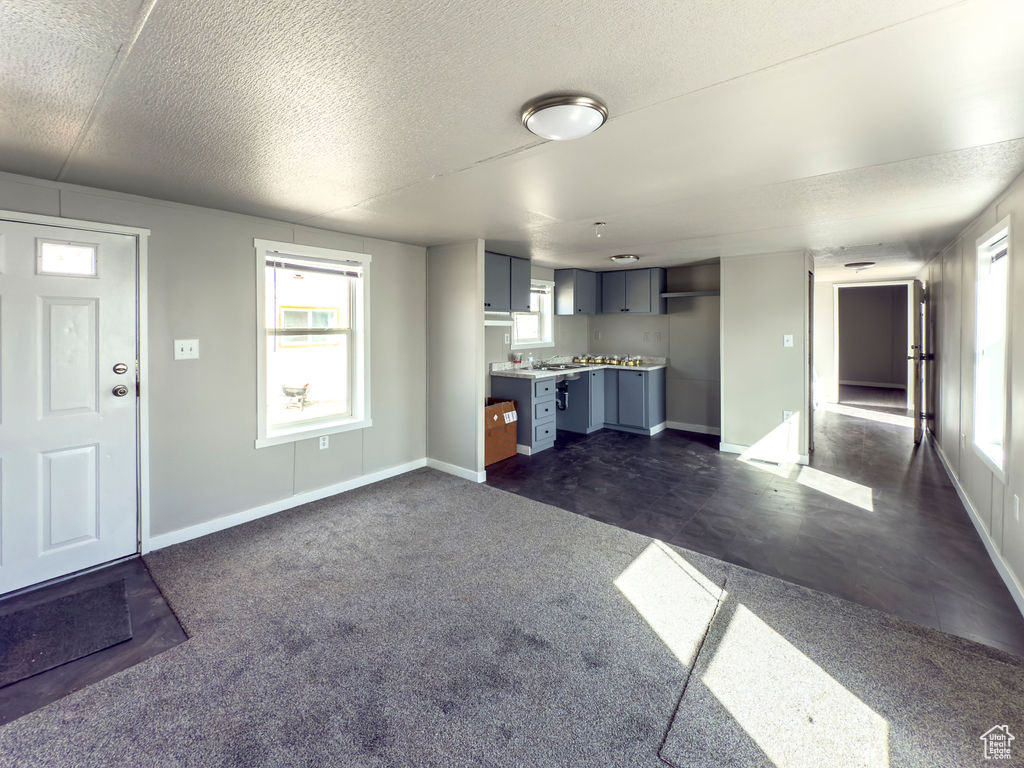 Unfurnished living room with baseboards, a textured ceiling, and dark colored carpet