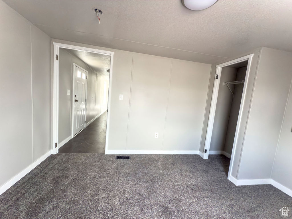 Unfurnished bedroom with dark colored carpet, a textured ceiling, baseboards, and a closet