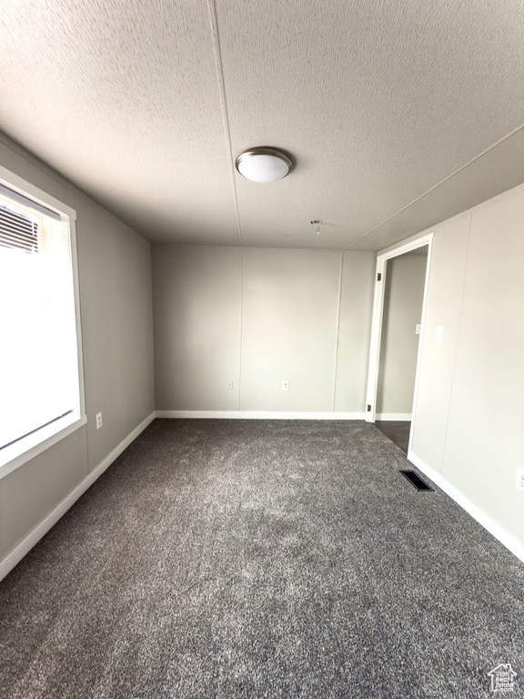 Carpeted empty room with a textured ceiling and baseboards