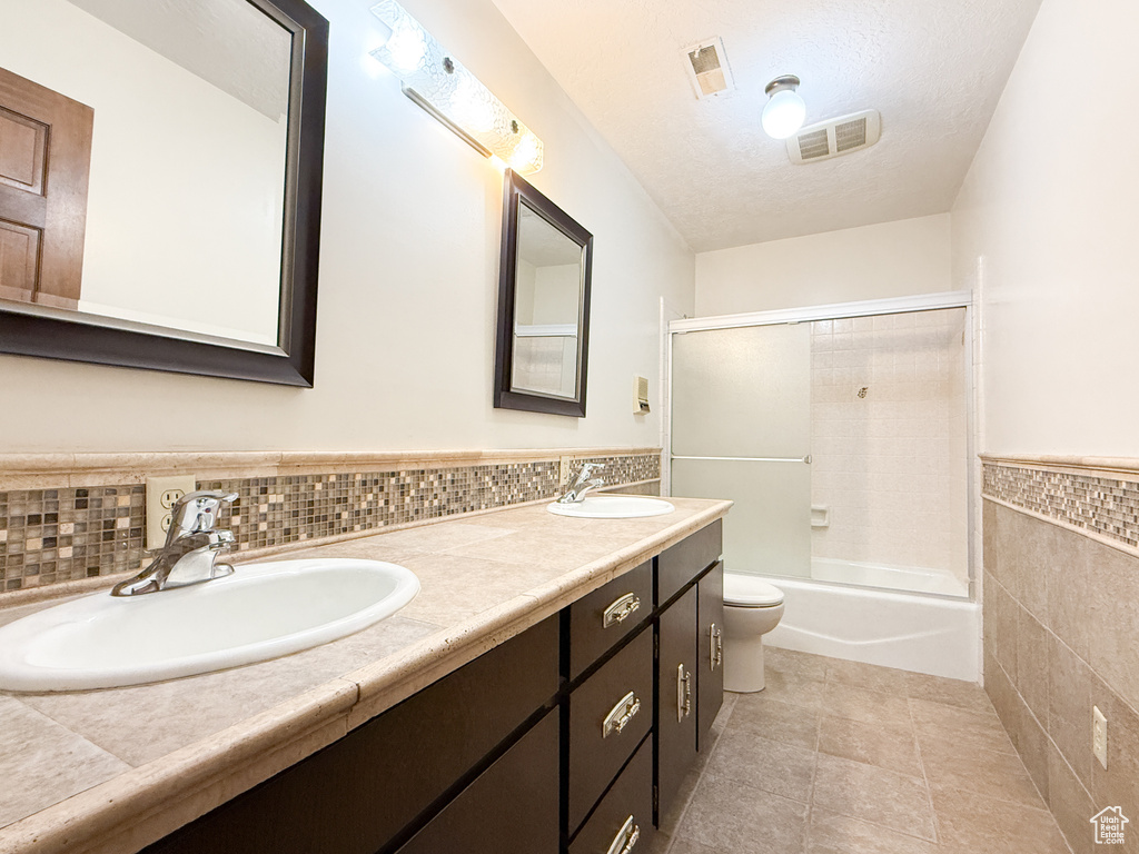 Bathroom with tile walls, tile patterned flooring, toilet, double vanity, and wainscoting
