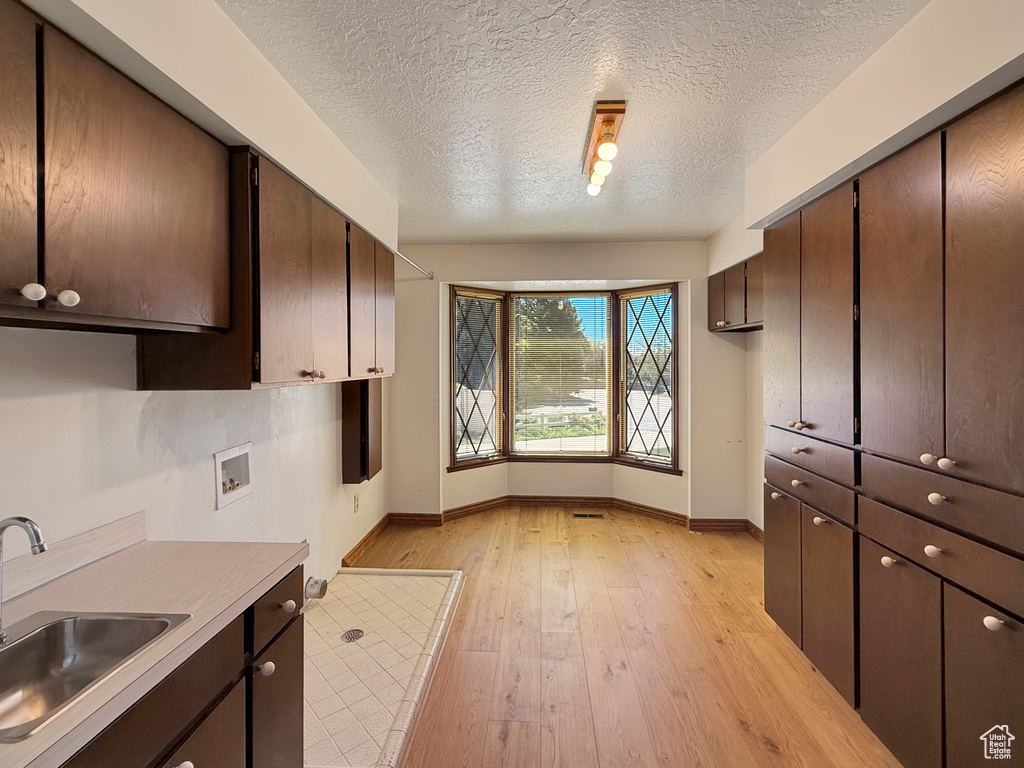 Kitchen with a sink, baseboards, light wood-style floors, light countertops, and a textured ceiling