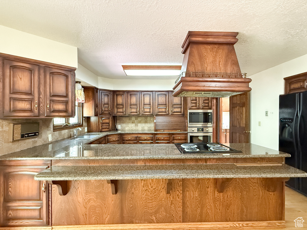 Kitchen with black appliances, dark stone counters, decorative backsplash, a sink, and a peninsula