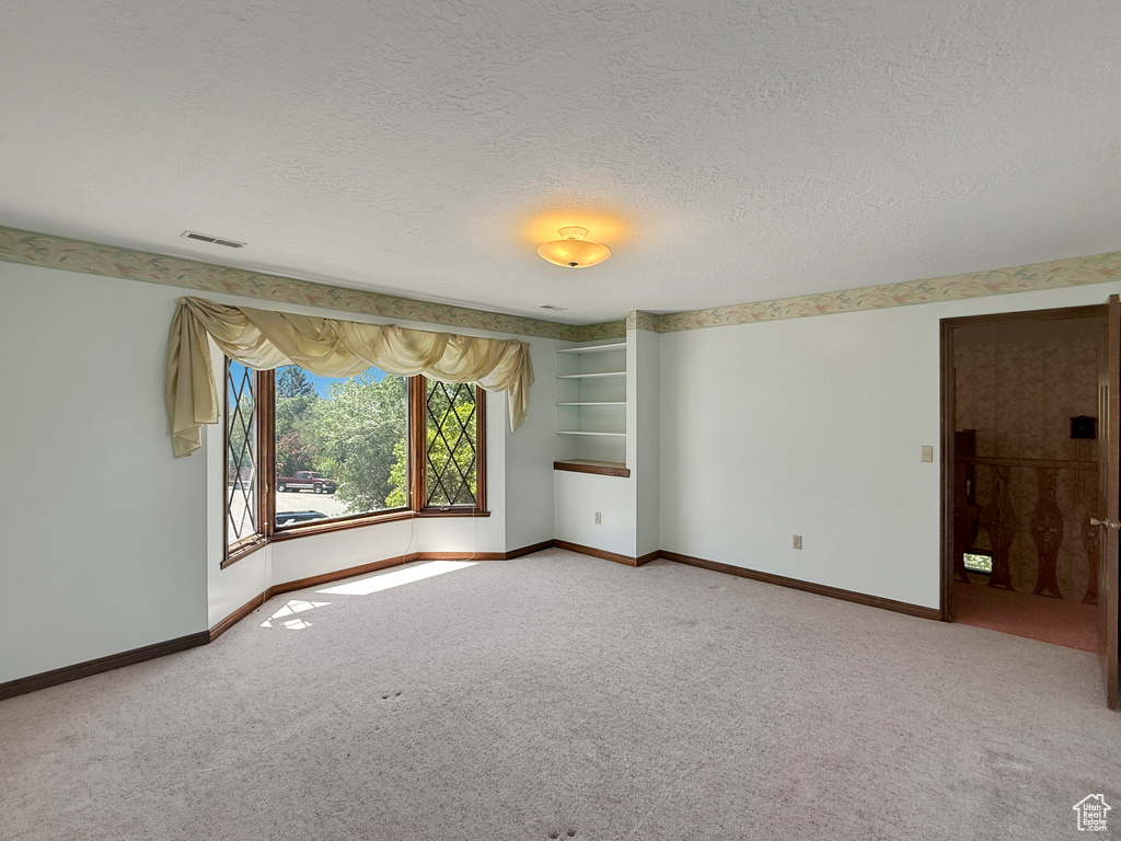 Empty room featuring light carpet, a textured ceiling, and baseboards
